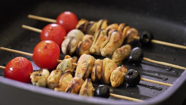 Grilling skewers with cherry tomatoes, mussels and black olives on a frying pan