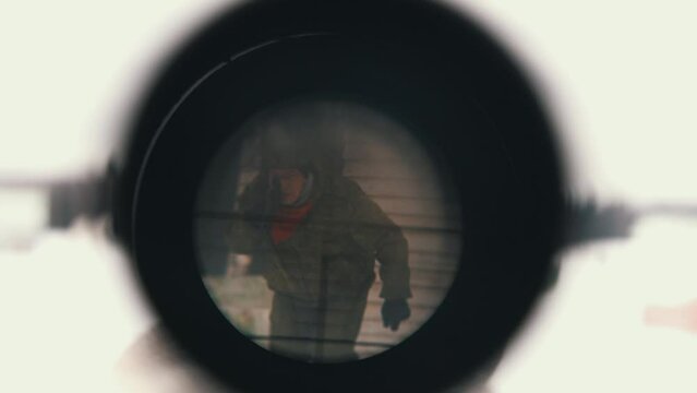 Man in army style clothing walks bending towards camera with magnifier lens in snowy field near blurry forest extreme close view