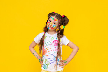 Happy little girl painted with colorful paints. A child with a stained face in paints, enjoys...