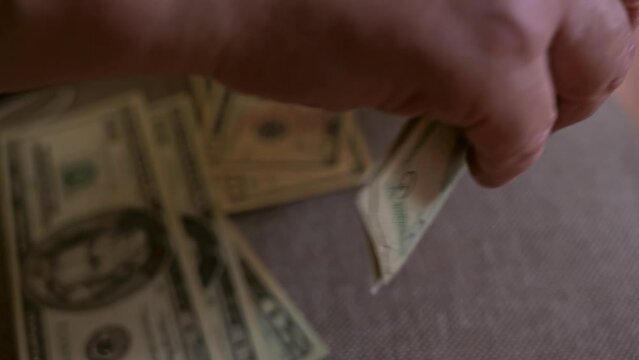 An elderly man is counting ten-dollar bills and twenty-dollar bills, close-up.