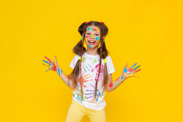 A little girl stained with multicolored paints. A happy, beautiful young girl painted with artistic paints. The child shows his smeared palms in paint and smiles. Yellow isolated background.