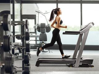 Fototapeta na wymiar Young woman running on a treadmill at a gym
