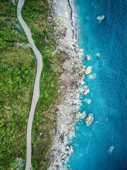 Aerial top view of a road along a green coastline against the sea waves