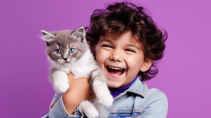 Little boy holds a kitten in his arms on purple background.