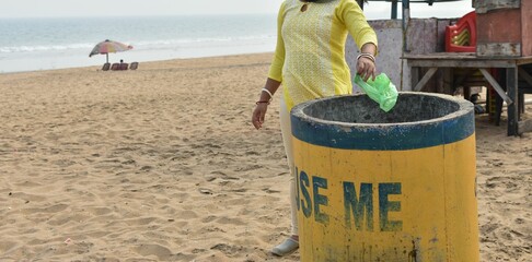 a woman throwing a plastic bag into a trash receptacle on the shoreline of Puri Beach