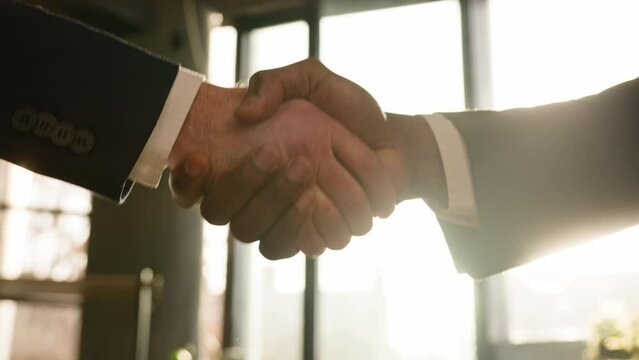 Close up male hands multiethnic Caucasian and African business people men diverse businessmen shaking successful corporate partnership deal union agreement hire handshake in office in sunny sun beams