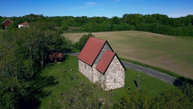Aerial footage over Berg Old Church (Berg steinkirke) with countryside and trees in Larvik, Norway