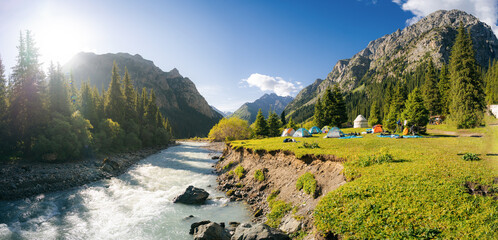 River and tent houses with yurt in the mountain valley of Altyn Arashan gorge, Kyrgyzstan. Morning vibes. Sun rays. Sunrise - obrazy, fototapety, plakaty