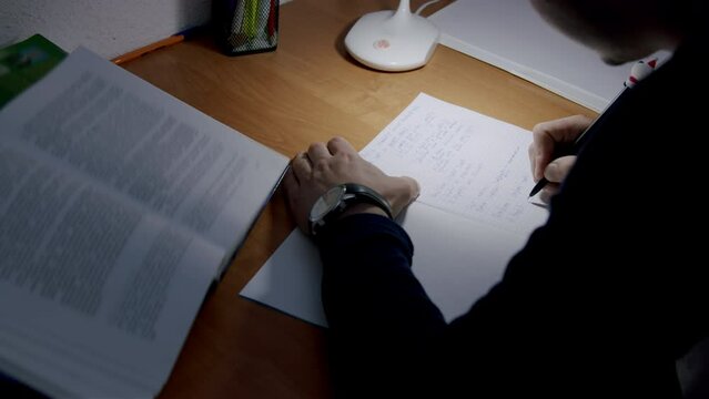 Student preparing to write his bachelor's thesis by the light of a lamp. Close-up image of a boy's hand writing down several ideas in a notebook and briefly sketching his material. Student concept