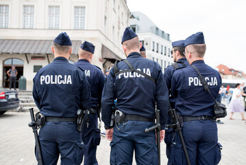 Polish policemen stand with their backs to the camera. - obrazy, fototapety, plakaty