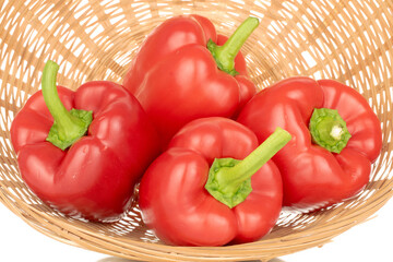 Several red bell peppers with straw plate, macro, isolated on white background.