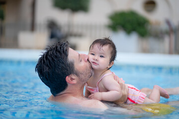 lifestyle portrait of father and little daughter enjoying summer - man holding her sweet baby girl excited and cheerful playing together at resort swimming pool in parenting concept