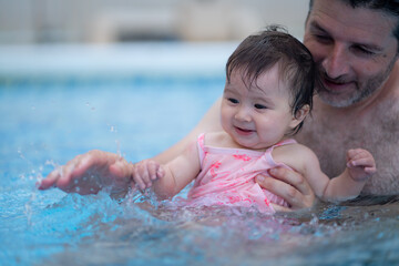 Fototapeta na wymiar lifestyle portrait of father and little daughter enjoying summer - man holding her sweet baby girl excited and cheerful playing together at resort swimming pool in parenting concept