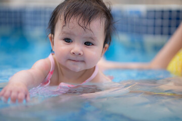 happy and beautiful Asian woman holding her little baby girl playful - Korean mother and adorable daughter playing on water at resort swimming pool in Summer