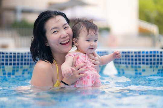happy and beautiful Asian woman holding her little baby girl playful - Korean mother and adorable daughter playing on water at resort swimming pool in Summer