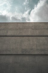 View of a street corner featuring a grey concrete wall and a bright blue sky with fluffy clouds.