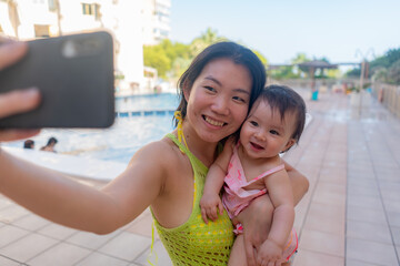 Asian woman taking selfie photo with her adorable baby girl - beautiful Chinese mother holding her...
