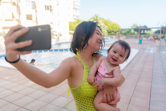 Asian woman taking selfie photo with her adorable baby girl - beautiful Chinese mother holding her little daughter and taking picture with mobile phone during holidays