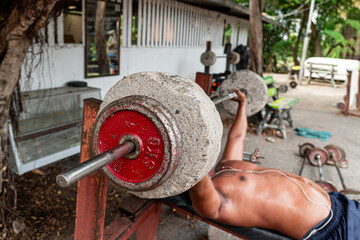 a man lifts a homemade barbell in an outdoor gym. The concept of sports for the poor. Old homemade...