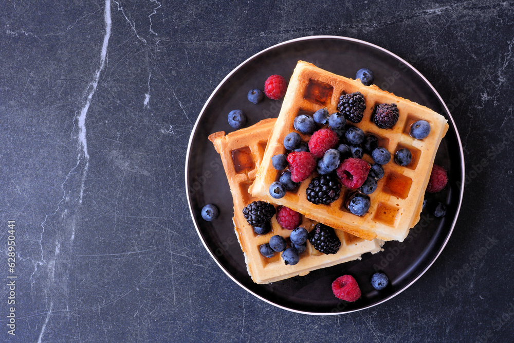 Poster breakfast waffles with raspberries and blueberries. above view over a dark stone background.