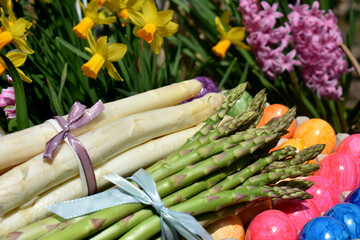 Grüner und weißer Spargel zusammen mit bunten Eiern an Ostern vor Frühlingsblumen