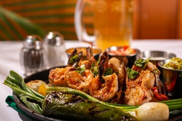 Closeup of a plate of freshly cooked vegetables and shrimp, with a glass of beer in the background