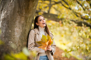 Beautiful girl outdoors in autumn fall. Young woman collects yellow fall leaves in autumn. Beauty woman holds autumn yellow leaf fall the face. Portrait of sensual woman over autumn fall background.