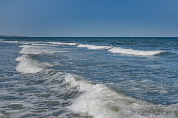 Waves rolling on the shore. The blue color of the sky is reflected in the water of the sea.