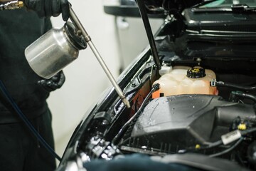 Worker wearing protective gloves is spraying a car engine with a can of cleaning solution