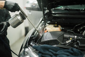 Worker wearing protective gloves is spraying a car engine with a can of cleaning solution