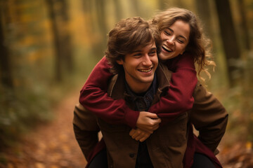 Fototapeta na wymiar Happy young man carrying his beautiful smiling pretty woman on his back at the park, having fun together. Boyfriend giving piggyback ride on shoulder to his beautiful girlfriend in autumn. High
