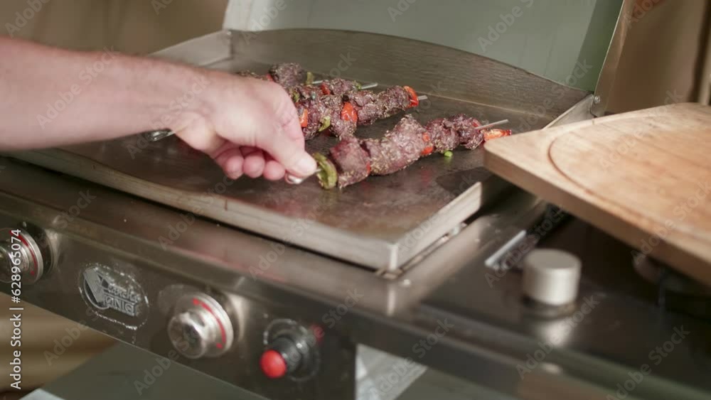 Poster Hand flapping shish kebab sticks on grill stove