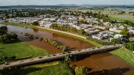 Scenic view featuring cars on the bridge over a river with buildings and trees surrounding the area
