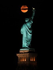 Vertical shot of the  iconic Statue of Liberty and a full moon at night
