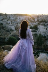 Young woman with long, flowing dress on a hilltop, admiring the majestic mountain range