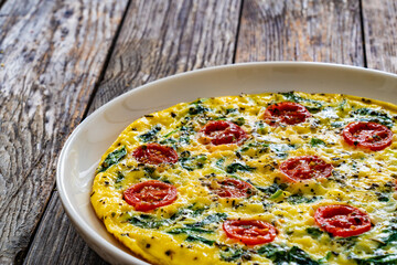 Delicious breakfast - scrambled eggs with spinach and cherry tomatoes on wooden table