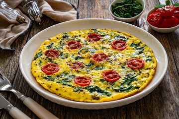 Delicious breakfast - scrambled eggs with spinach and cherry tomatoes on wooden table