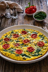 Delicious breakfast - scrambled eggs with spinach and cherry tomatoes on wooden table