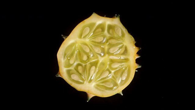 Sliced Kiwano cucumber rotating on a black background, gradually fading into shadow.