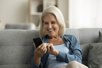 Happy retired senior woman using medical service, healthcare application on digital gadget at home, typing on smartphone, smiling, laughing at screen, enjoying Internet connection
