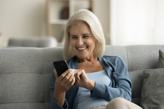 Happy Retired Senior Woman Using Medical Service, Healthcare Application On Digital Gadget At Home, Typing On Smartphone, Smiling, Laughing At Screen, Enjoying Internet Connection