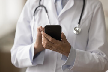 Cropped shot of doctor woman in uniform coat using medial application on smartphone for online...