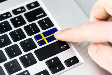 Online International Business concept: Computer key with the Sweden on it. Male hand pressing computer key with Sweden flag