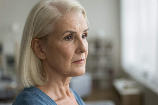 Serious pensive senior woman looking at window away in deep thoughts, thinking over problem solution, trouble, retirement, disease, feeling lonely. Thoughtful blonde elder lady casual portrait
