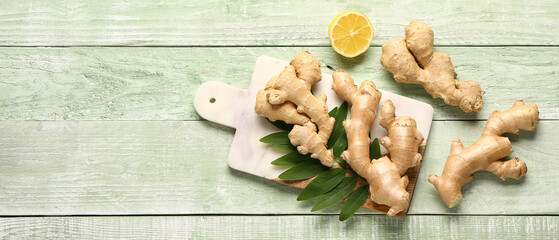 Board with fresh ginger roots and half of lemon on green wooden background with space for text