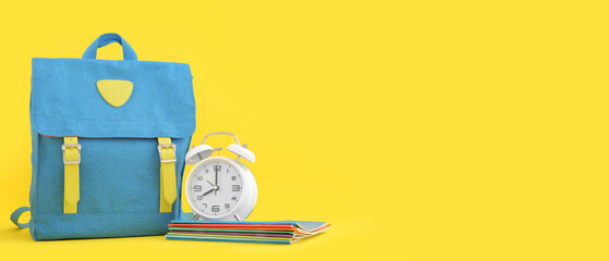 Alarm clock with backpack and copybooks on yellow background with space for text