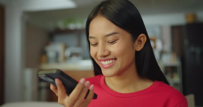 Young asian woman using voice search on smartphone in living room at home. She enjoy vocal order to help chatbot or social media.