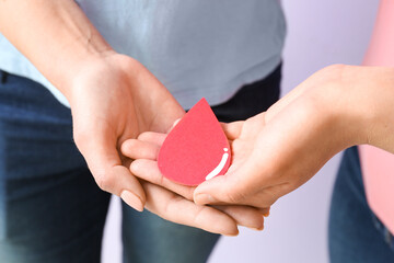 Women with paper blood drop on lilac background, closeup. World Donor Day