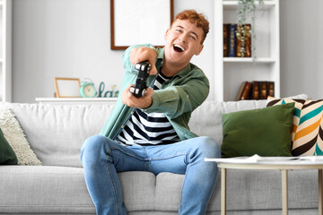 Young redhead man playing video game at home