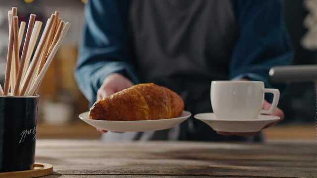 The client, an expert barista, responsibly receives an order of coffee and croissant from coffee bakery. bartender-coffee maker is engaged in service showing his skill in making coffee Online shopping
